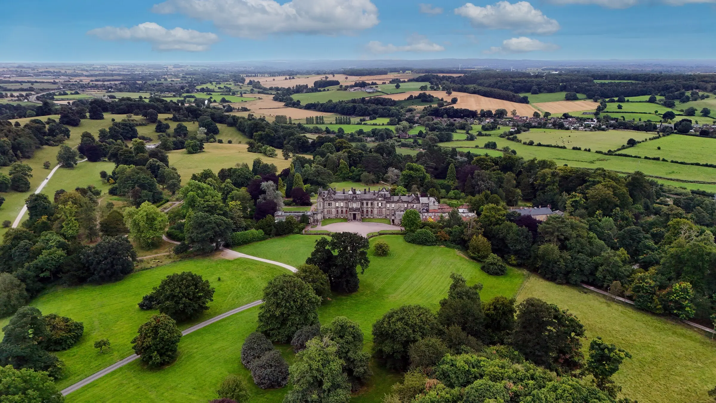 Aerial view of a country estate with mown parkland, specimen trees and hedged farmland beyond
