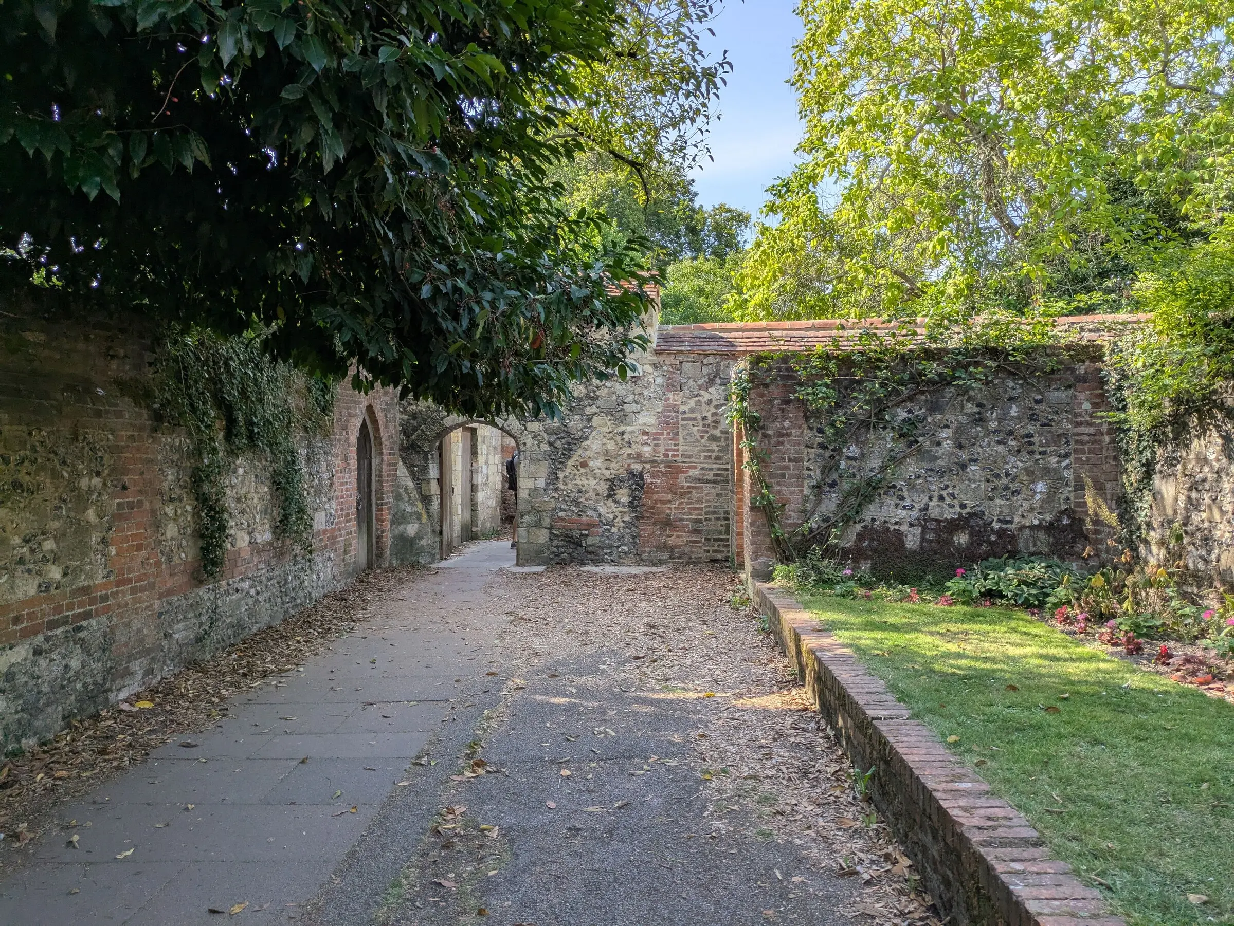 Red brick and knapped flint garden wall with clay tile coping running to an arched opening